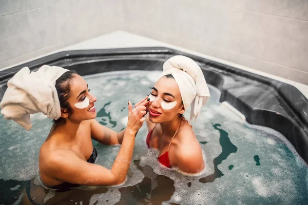 Joyeux et positif jeune modèle mettre un oeil sur ses amis asiatiques visage. Tous les deux sourient. Modèles assis dans un jacuzzi plein d'eau . — Photo