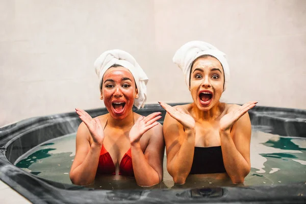 Çok mutlu genç kadın Jakuzi su dolu oturup ve kameraya bak. Onlar hayret ve hayrandı. Güzellik maskeleri modelleri var.