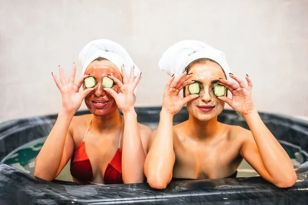 Komik genç kadın jakuzide oturun ve salatalık parçaları gözünü tutun. Onlar güzellik yordamlar ve spa odasında olduğunu. Modelleri mutlu görünüyorsun.