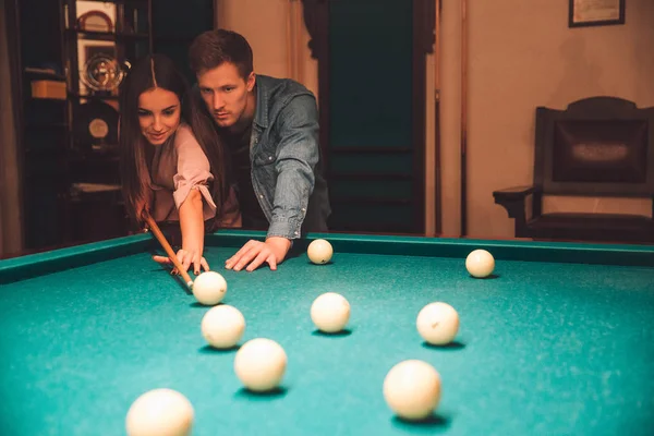 Young man and woman stand together in billiard room. He teach her how to aim into billiard ball. They dating. — Stock Photo, Image