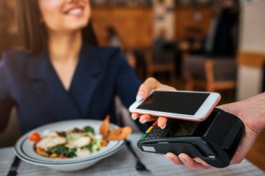 Neşeli genç müşteri masasına oturup garson bak. O gülümseme. Model telefon terminal üzerine tutun. Öğle yemeği için öder