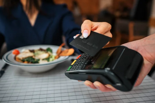 Primer plano de la tarjeta de retención del cliente cerca de la terminal. Ella paga por comer en el restaurante. Ensaladera de pie en la mesa . — Foto de Stock