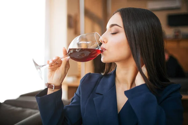 Picture of young woman drinking red wine from glass. She keep eyes closed and enjoy. Model hold one hand on neck. — Stock Photo, Image