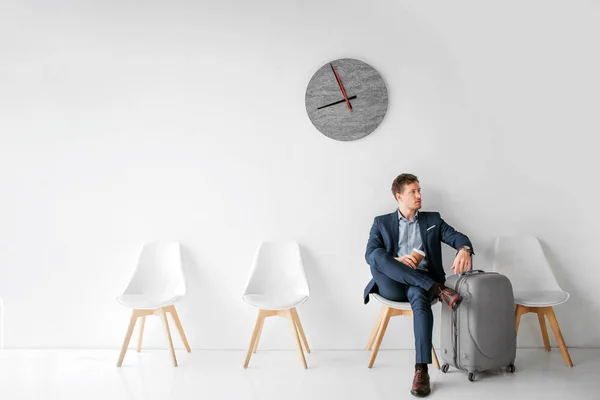 stock image Serious young man sit on white chair and look to right. He hold one leg on another. Guy wait for flight.