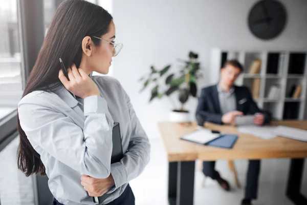 Härlig bild av unga självsäkra kvinnan titta tillbaka på hennes chef. Han sitter vid bordet. Guy titt på modellen. Hon berör håret med sexuell flytta. — Stockfoto