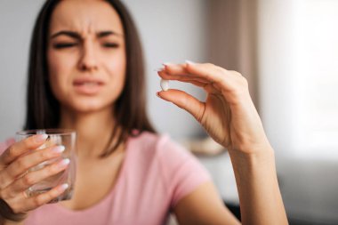 Genç güzel model parmak arasında beyaz hap tutun ve ona bak. O su vardır. Modeli hap ile su içmek gerekir. O küçülür. Genç kadın acı.