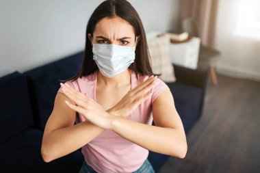 Ciddi genç kadın koltukta otur. Ağız maskesi ile kaplı. Modelleri çok hasta. O eliyle dur işareti gösterir. Genç kadın kızgın.