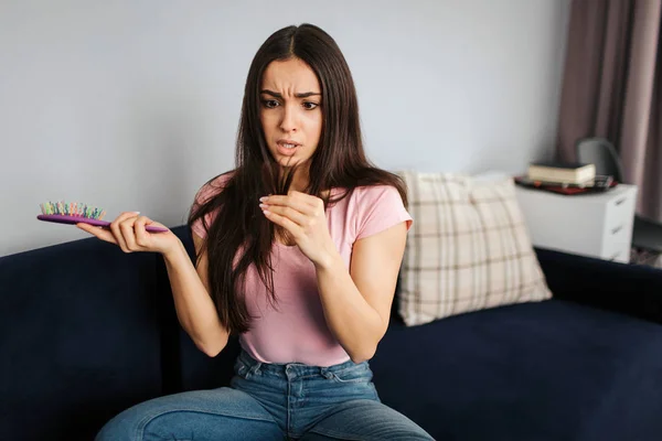 Jovem infeliz e chateada, olhe para o cabelo. Ela tem problemas com isso. Modelo segurar escova de cabelo na mão . — Fotografia de Stock