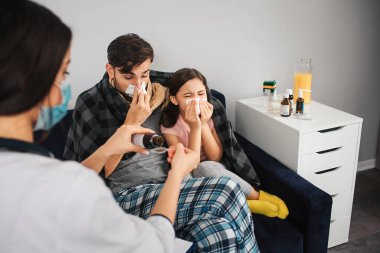 Genç adam kızı koltukta oturan ve hapşırma ile resmi. Soğuk yakaladılar. Kadın doktor şurubumu kaşık dökme.