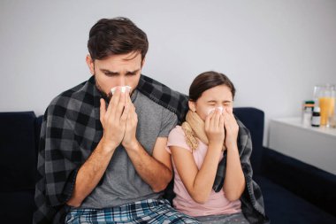 Küçük kız yatak ve beyaz doku hapşırma ile genç adam sit. Soğuk yakaladılar. Aile battaniye ile örtülü.