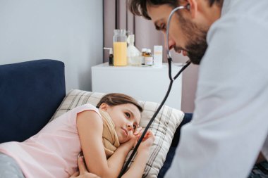 Hasta küçük kız yatakta yatıyordu. Genç doktor stetoskop ile onun nefesini dinle. O onun içinde oda besdies oturmak.