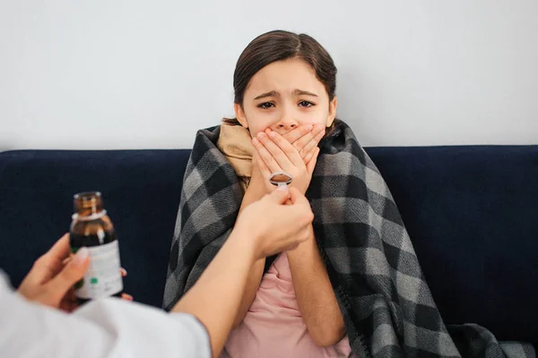 Small girl look on camera and cover mouth with hands. She is frightened. Female doctor give her spoon with syrup. Girl doesnt want to open mouth. — Stock Photo, Image