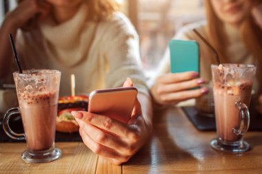 İki genç kadın kesme görünümünü tutuşsun telefonları. Bakmak yok. Younf kadınlar içinde masaya oturabiliriz. Gözlüğüm çikolata cocktais ile masaya.