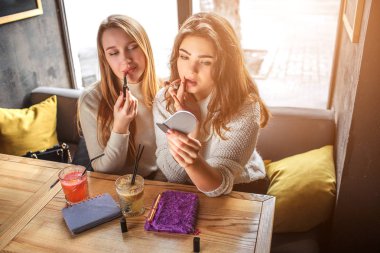 Dudaklarında ruj koyarak iki genç güzel modeller. Arada bir aynaya bak. Kızlar içinde kafede oturup