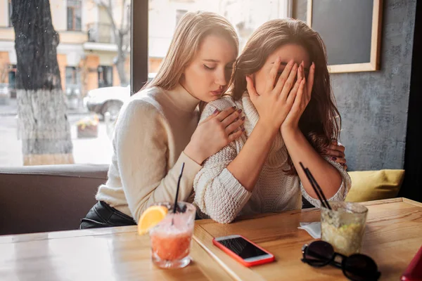 Die aufgebrachte Brünette sitzt am Tisch und bedeckt das Gesicht mit den Händen. ihr Freund versucht sie zu trösten. — Stockfoto