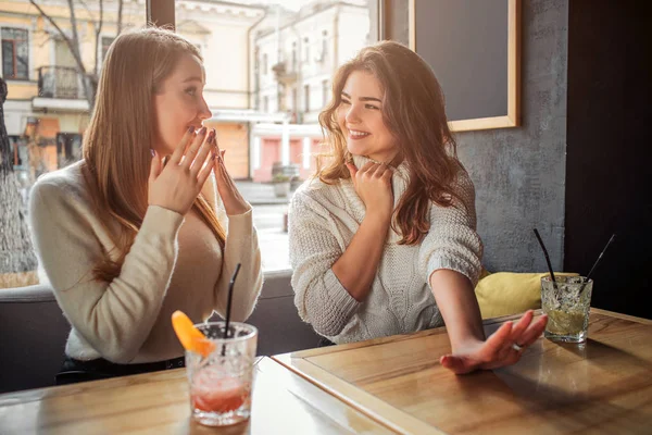 Fröhliche und fröhliche junge Frauen sitzen am Tisch. Erste Hand zeigen. fragt sich ein anderes Modell. Sie sind glücklich. — Stockfoto