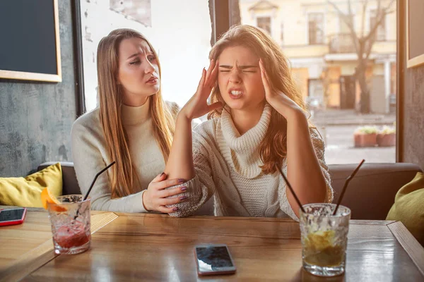 Angry young man hold hands on head. She has headache. Her friend sits besides her and trry to comfort. Brunette is irritated. — Stock Photo, Image
