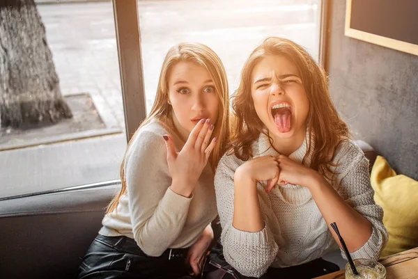 Two young women makes funne faces. They grimace. Blonde model cover mouth with hand.