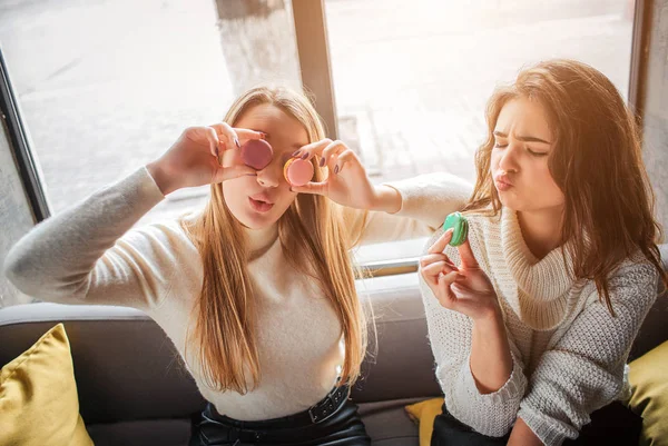 Verspielte junge Frauen essen Macarons und bedecken die Augen damit. Sie haben Spaß zusammen. — Stockfoto