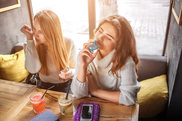 Junge Frauen sitzen am Tisch und riechen Parfüm. Brünette hält blaue Flasche. sie haben Ruhe und Entspannung. — Stockfoto