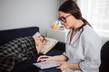 Yatak odasında yatan hasta bir küçük kız. Kadın doktor onu yanı sıra oturup bakmak.