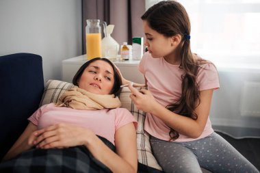 Kanepede yatan hasta bir genç kadın. Boğazını eşarp tarafından sarılır. Kız yanında otur ve boğaz spreyi tutun. Genç kadın göz.