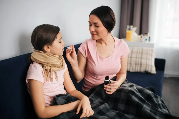 Beteg lány ül, valamint az anyja. Tartsa a nyitott száj, és kap a szirup kanállal. Fiatal nő hold üveg. Ő ül együtt gyermek heverő. — Stock Fotó