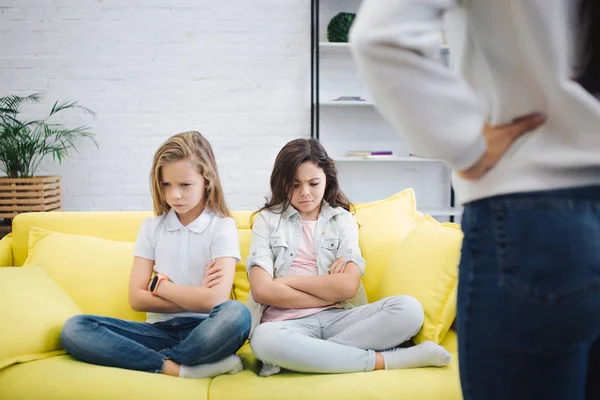 Sad and upset teenagers sit on sofa in room and look down. They hold hands and legs crossed. Young woman stand in front of them. She hold hands on hips. — Stock Photo, Image