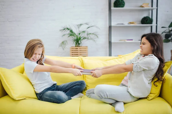 Két tizenéves sárga kanapé szobában ülni. Fenyő notebook harcolnak. Minden lány húzza magát. Küzdenek. — Stock Fotó