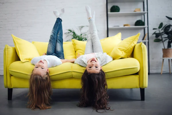 Divertenti giovani adolescenti sdraiati sul divano giallo e guardando dritto sulla macchina fotografica. Sorridono. Le ragazze tengono le gambe in aria. I loro capelli toccano pavimento . — Foto Stock