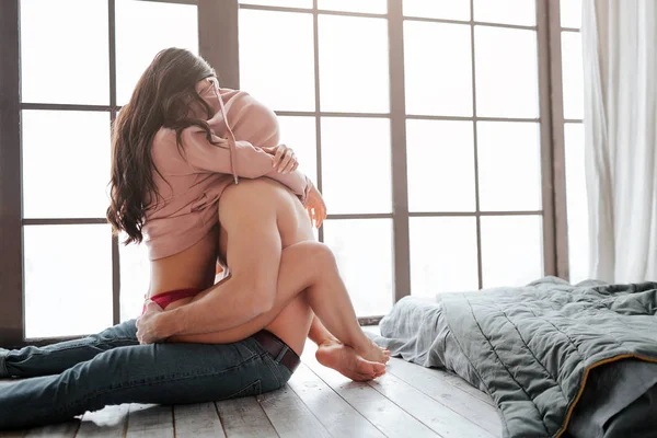 Sexy hot couple sit on floor in room. They hide heads under sweater. Young woman sit on man and embrace him with legs and hands. — Stock Photo, Image