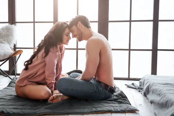 Romantic couple sit on floor in room. They touch each others foreheads and smile. People hold eyes closed.