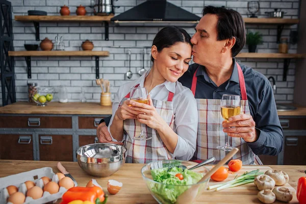 Güzel resim kadınla birlikte mutfakta masada oturan adam. Alnına öpücük ve cam şarap elinde tut. kadın ona yalın ve keyfini çıkarın. — Stok fotoğraf