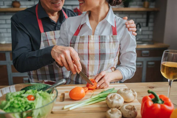 Erkek ve kadın stand görünümünü mutfakta masada birlikte ve pişirme kesti. O bıçak ve kesilmiş domates vardır. O ellerle kırmızı sebze tutun. Birbirinize bakın ve gülümse. — Stok fotoğraf