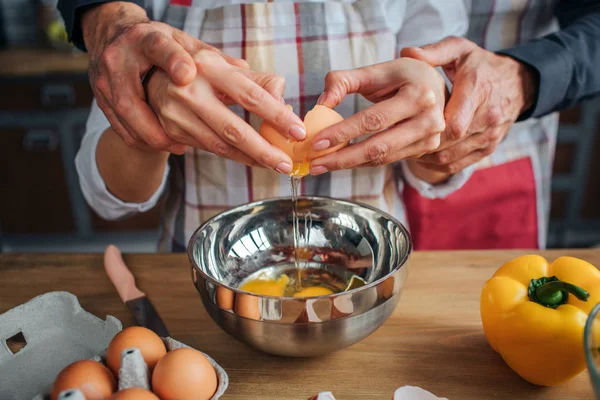 Närbild av mannen andwoman händer att bryta ägg tillsammans. De gör det över metall skål. Ägg med peppar och kniv stå på bordet. — Stockfoto