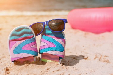 Kum plaj Flip-flop. Üzerine güneş gözlüğü. Yaz tatil kavramı. Deniz kıyısında. Cennet. Pembe yüzme yüzük arkasında kum üzerinde yalan.