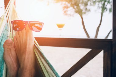 Güneşli bir plaj okyanus tarafından adlı bir hamakta yatan genç adam. Ayakları üzerinde güneş gözlüğü.