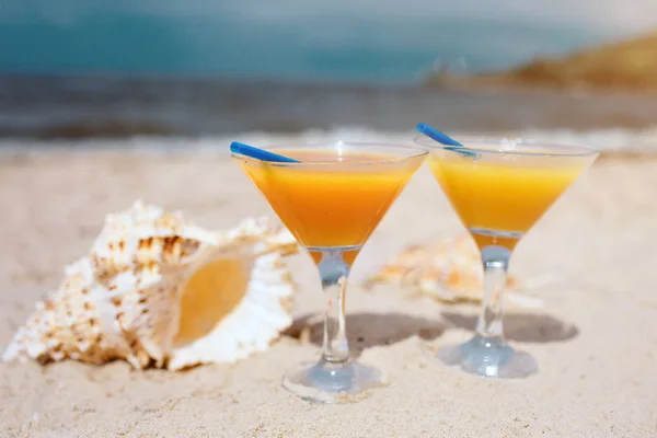 Sommerkonzept: frische, orangefarbene Cocktails am Strand. schöne weiße Schale, die daneben auf Sand liegt. Die Sonne scheint hell. horizontale Lergesicht. Paradies. — Stockfoto