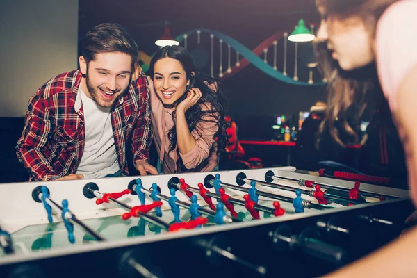 Jóvenes estudiantes jugando futbolín juntos en la habitación. Hombre oponente a mujer. Ellos emocionados y juguetones . — Foto de Stock