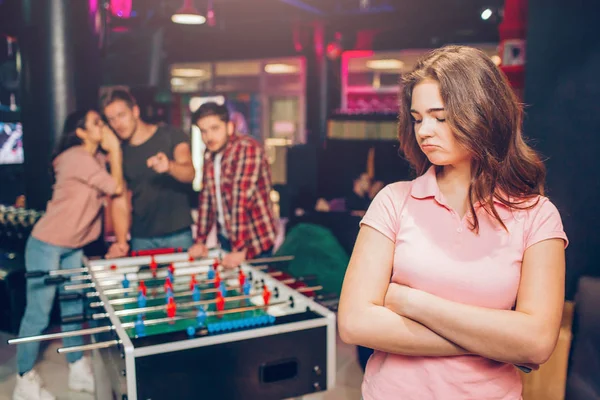 Jonge vrouw in roze hemd staan op de voorgrond. Ze houden de handen gekruist. Model verstoren. Haar vriend roddel van haar maken. Ze praten en wijs. — Stockfoto