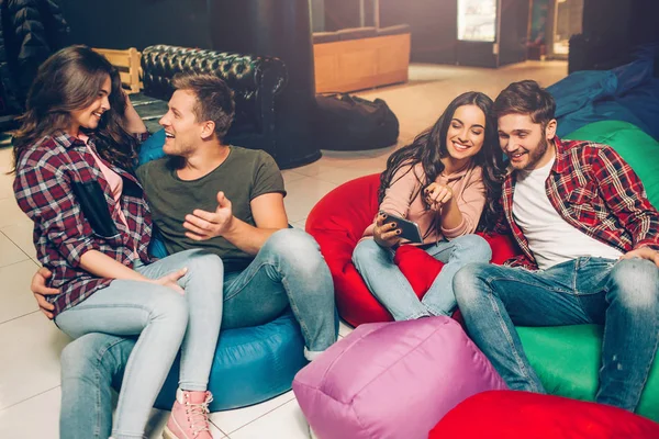 Deux couples assis sur des sacs gonflables dans la salle de jeux. D'abord, parlez-vous. deuxième regard sur téléphone en brunes mains . — Photo