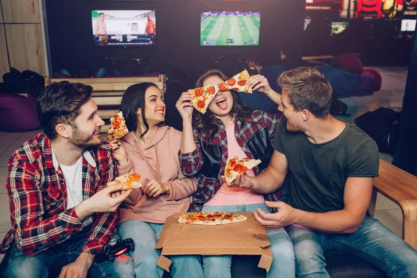 Funny young people sit together in room and eat pizza. They play with its pieces. Teammates laughing. — Stock Photo, Image