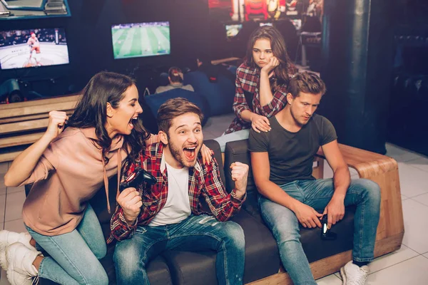 Picture of happy couple cheering while second is upset. They win and lost game. Guys hold gamepads in hands. They sit together in playing room. — Stock Photo, Image