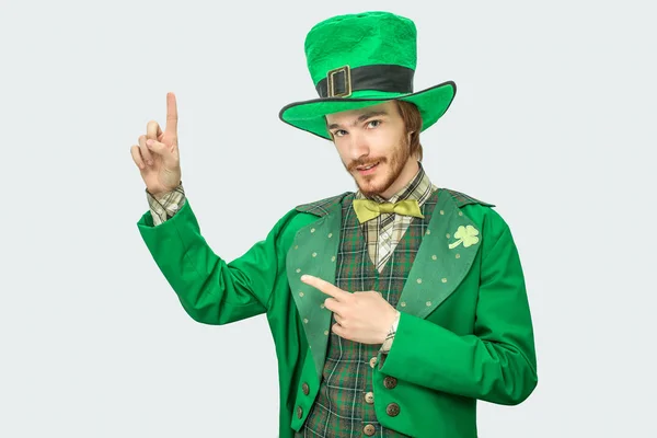 Bonito joven en traje verde mirar a cámara y apuntar hacia arriba. Lleva el disfraz de Patricks. Aislado sobre fondo gris . — Foto de Stock