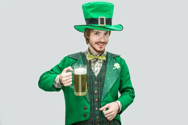 Boldog fiatalember zöld Szent Patricks öltöny gazdaság bögre sört. Úgy néz ki, a kamera és a mosoly. A srác, magabiztos és pozitív. Elszigetelt zöld háttér. — Stock Fotó