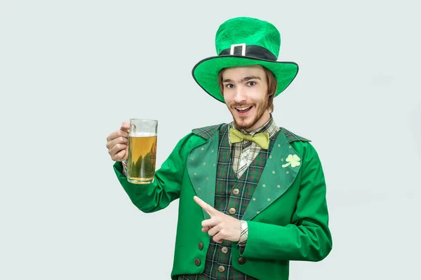 Boldog, vidám fiatal férfi zöld saint patick öltöny kezében korsó sör és Nézd meg a kamera. Ő pont és a mosoly. Elszigetelt, a szürke háttér. — Stock Fotó