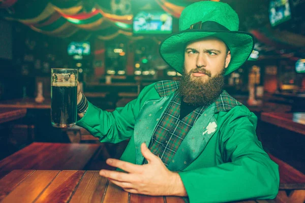 Zöld St. Patricks megfeleljen a részeg fiatalember kocsmában asztalnál ülni. Ő ragaszkodik bögre barna sör. A fickó hűtés. — Stock Fotó