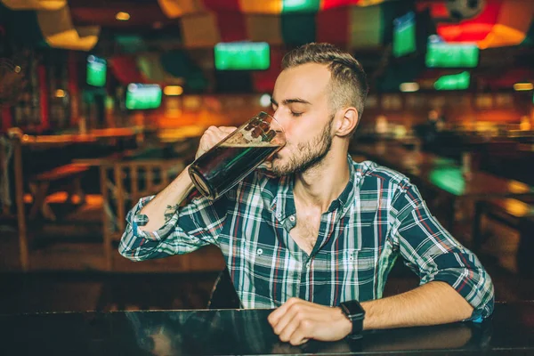 O jovem senta-se sozinho no balcão do bar no pub. Ele bebe cerveja escura da caneca . — Fotografia de Stock