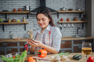 Mutfak masasında güzel esmer sit. Dur ve bak. Kadın gülümseme. Sebze ve şarap kadehi masaya vardır.