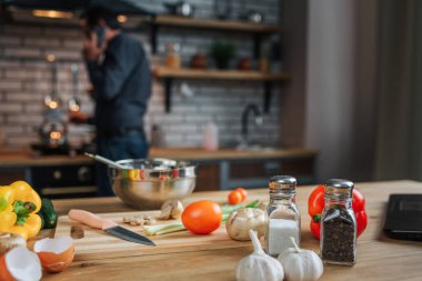 Renkli iyi sebze ve baharat masada. Yetişkin adam, ayakta ileri soba ve yemek pişirmek. Telefon adam konuşma.